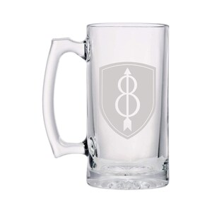 Puede incluir: Un jarro de cerveza de vidrio transparente con asa. El jarro tiene un escudo gris con una flecha blanca y el número 8 en su interior.