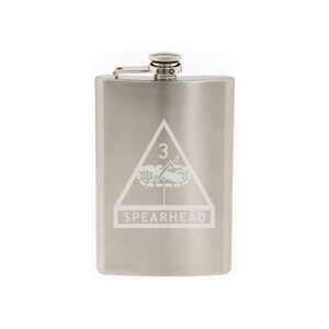 May include: A silver stainless steel flask with a white engraved design of a triangle with the number 3 inside, a lightning bolt, and the words "SPEARHEAD".