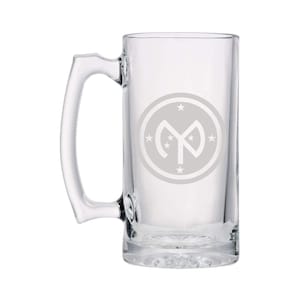 May include: A clear glass beer stein with a handle. The stein has a white etched design of a circle with a star inside and the letter "M" in the center.