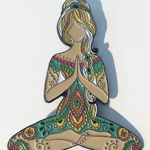 May include: A colourful enamel pin depicting a woman in a lotus pose with intricate patterns and designs. The woman has long, flowing hair and is wearing a green and orange outfit.