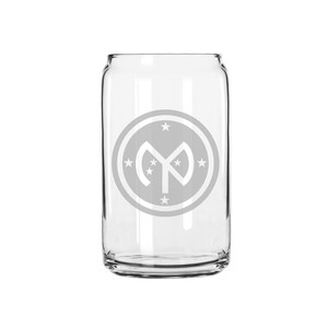 May include: A clear glass can with a white etched design of a circle with a star inside and a stylized letter "M" with stars around it.