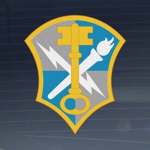 May include: A gold key with a torch and lightning bolt crossed behind it, all on a blue and gray shield with a yellow border.