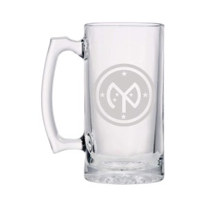 May include: A clear glass beer stein with a handle. The stein has a white etched design of a circle with a star inside and the letter "M" in the center.