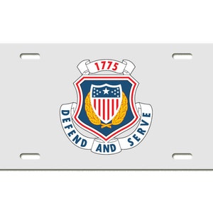 May include: White metal license plate with a blue and gold shield with a red and white American flag inside. The shield is surrounded by a white banner with the text "DEFEND AND SERVE" and a smaller banner with the text "1775".