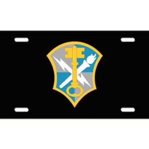 May include: Black license plate with a gold, blue, and gray shield featuring a key, lightning bolt, and torch. The shield is the emblem of the United States Army.