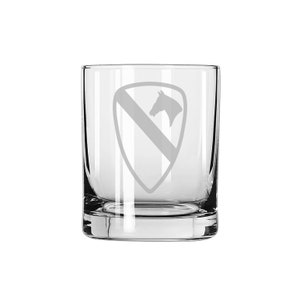 May include: A clear glass tumbler with an etched design of the 1st Cavalry Division insignia, featuring a horse's head and a shield with a diagonal stripe.