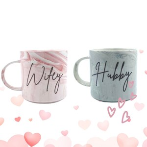 K&ouml;nnte beinhalten: Zwei Keramikbecher mit marmorierten Mustern. Der rosa Becher sagt "Wifey" und der graue Becher sagt "Hubby".