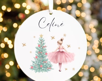 May include: Round white Christmas bauble with a ballerina and Christmas tree design. The bauble has the name "Celine" in cursive script. The ballerina wears a pink tutu. Gold stars are scattered around the design.