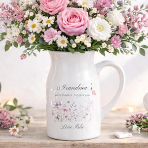 Könnte beinhalten: Eine weiße Keramikkrug gefüllt mit einem Strauß rosa und weißer Blumen, darunter Rosen und Gänseblümchen. Der Krug hat einen Henkel und den Text: „If Grandma's were flowers, I'd pick you. Love Isla.“