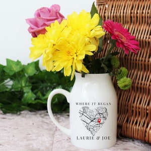 May include: White ceramic milk jug with a black and white map design in the shape of a heart. The map has a red pin in the center. The text "Where it began" is above the map and "Laurie & Joe" is below the map.