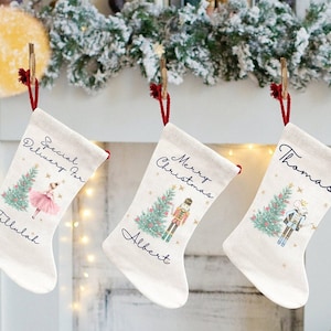 Könnte beinhalten: Drei weiße Weihnachtsstrümpfe mit rotem Besatz und personalisierten Namen. Die Strümpfe zeigen einen Weihnachtsbaum, eine Ballerina und einen Nussknacker.