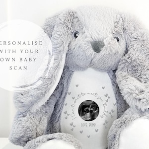 May include: A plush gray bunny rabbit with a white belly. The belly features a baby scan image, surrounded by the text "I can't wait to meet you, baby" and "Love Bump". The text "Personalise with your own baby scan" is also visible.