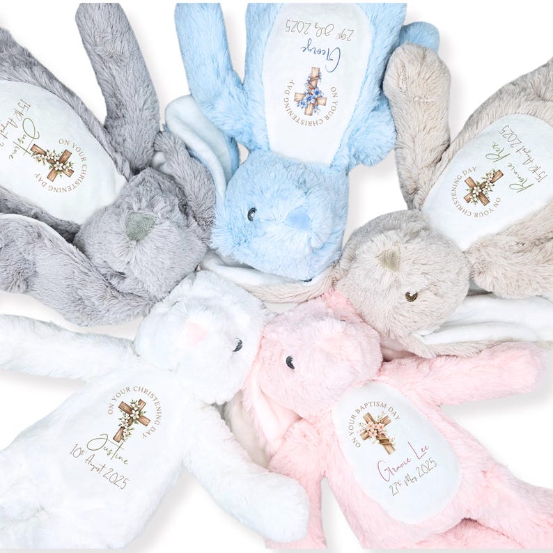 Op de afbeelding: Een verzameling pluche konijnen in pastelkleuren, waaronder grijs, blauw, wit en roze. Elk konijn heeft een gepersonaliseerde geborduurde patch met een kruis en tekst, inclusief namen en data, waarschijnlijk voor een doop.