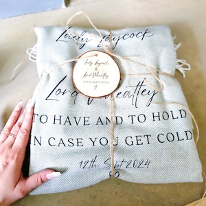 May include: A light blue blanket wrapped with twine and a wooden tag that reads "Lady Laycock & Lord Wheatley 12th Sept 2024" and "Long & Wheatley To Have And To Hold In Case You Get Cold 12th Sept 2024".
