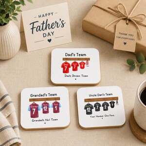 Op de afbeelding: Drie vierkante witte onderzetters met gepersonaliseerde illustraties van sportshirts die aan een houten rek hangen. Elke onderzetter toont namen en nummers op de shirts, met teksten zoals Dad's Team, Grandad's Team en Uncle Dan's Team.