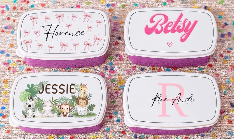 May include: Four personalized lunch boxes with white lids and purple bases. The lids feature names and designs: "Florence" with bows, "Betsy" with a heart, "Jessie" with jungle animals, and "Rue Andi" with an initial.