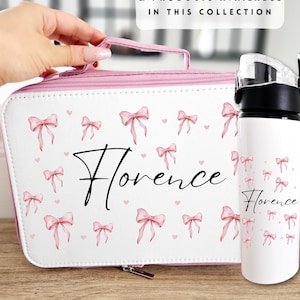 Pode incluir: Um conjunto de bolsa de cosméticos e garrafa de água brancos com um padrão de laços rosa e o nome "Florence" em escrita preta. A bolsa tem uma alça e acabamentos rosa. A garrafa tem uma tampa preta.