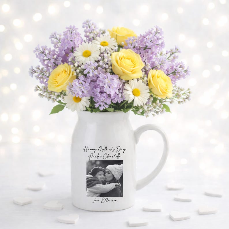 May include: A white ceramic pitcher with a handle, filled with a bouquet of yellow roses, white daisies, and purple lilacs. The pitcher has a black and white photo and text that reads "Happy Mother's Day Auntie Charlotte" and "Love Ellie xxx".