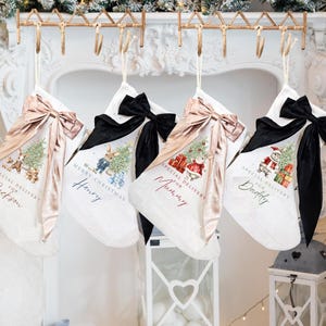 May include: Four white Christmas stockings with decorative bows and personalized text. Each stocking features a different design, including a Christmas tree, gifts, and festive characters. The stockings are labeled "Jackson", "Henry", "Mummy", and "Daddy".