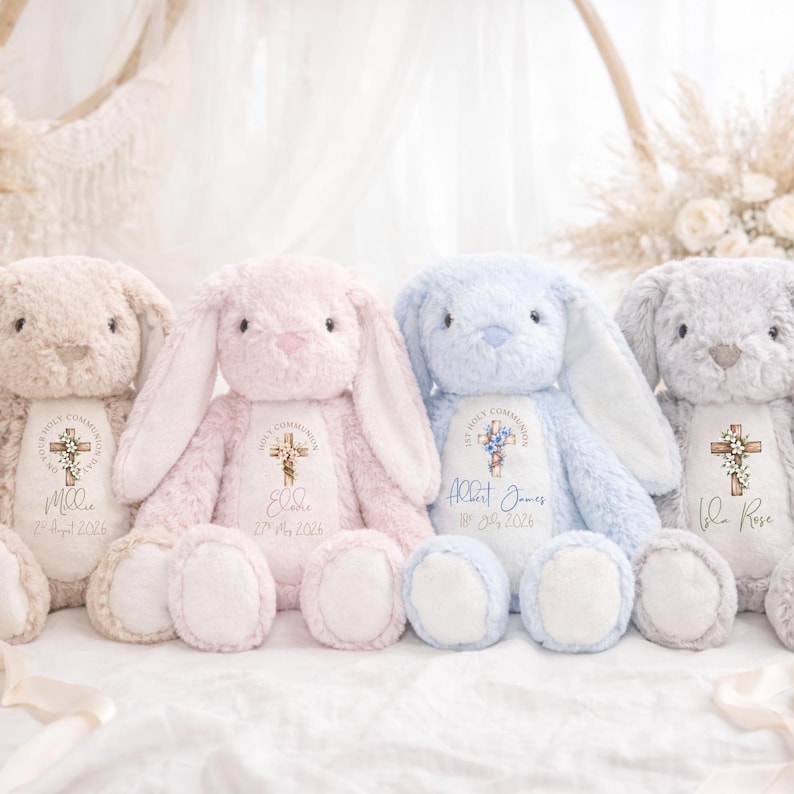 May include: Four plush stuffed bunnies in beige, pink, blue, and gray. Each bunny features a white chest patch printed with a cross, floral accents, and personalized text including names and dates for a First Holy Communion celebration.
