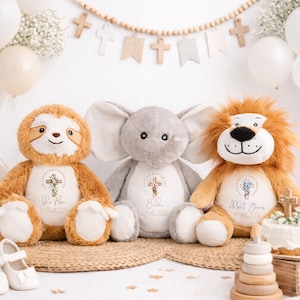Op de afbeelding: Drie pluche dieren: een luiaard, een olifant en een leeuw. Elk heeft een gepersonaliseerd geborduurd ontwerp met een kruis en tekst. De luiaard is bruin, de olifant is grijs en de leeuw is bruin met een pluizige manen. Ballonnen en decoraties op de achtergrond.