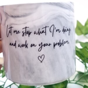 K&ouml;nnte beinhalten: Wei&szlig;e Keramiktasse mit Marmormuster und schwarzem Text, der "Lass mich aufh&ouml;ren, was ich tue, und an deinem Problem arbeiten." Ein kleines Herz befindet sich unter dem Text.