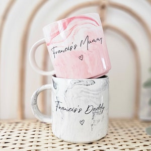 May include: Two ceramic mugs with marbleized designs. The top mug is pink with the text "Francis's Mummy" and a small heart. The bottom mug is gray with the text "Francis's Daddy" and a small heart.