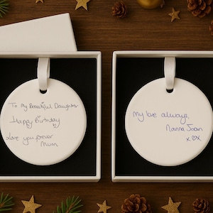 May include: Two white, circular ornaments with handwritten messages in black ink, displayed in square gift boxes. One says "To My Beautiful Daughters, Happy Birthday, Love you forever Mum." The other says "My love always, Nanna Joan xOX."