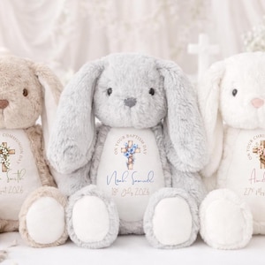Op de afbeelding: Drie pluche konijnen in beige, grijs en wit. Elk konijn heeft lange oren en een zacht, knuffelig uiterlijk. Ze hebben gepersonaliseerde geborduurde details met een kruis en tekst, inclusief namen en data, voor een doop of communie.