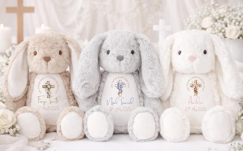 Op de afbeelding: Drie pluche konijnen in beige, grijs en wit. Elk konijn heeft lange oren en een zacht, knuffelig uiterlijk. Ze hebben gepersonaliseerde geborduurde details met een kruis en tekst, inclusief namen en data, voor een doop of communie.