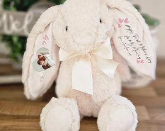 May include: A beige plush bunny with a white satin bow. The bunny has pink hearts and the text "Happy First Mother's Day to My Mummy Love Amelia xx" embroidered on one ear. A photo is visible in a heart-shaped frame on the other ear.