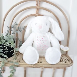 May include: White plush bunny with long ears, sitting on a woven chair. The bunny has pink embroidered details and a message that reads "hanna Alice Because someone we love is in heaven There's a little bit of heaven here with us".