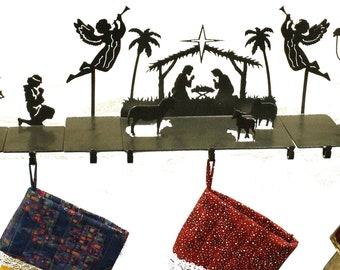 May include: A black metal Christmas stocking holder featuring a nativity scene silhouette with angels, shepherds, and the three wise men. Three Christmas stockings with colorful patterns hang below the metal scene, ready for the holidays.