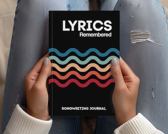 May include: A black songwriting journal with the text "Lyrics Remembered" and a colorful wave design. The journal is being held by a person wearing blue jeans.