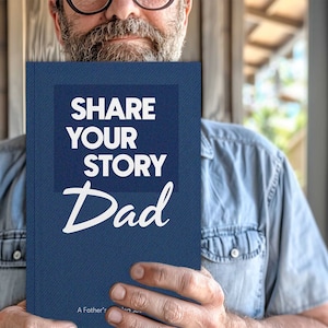 May include: A blue book with the text "Share Your Story Dad" in white lettering. The book is held by a person's hands.