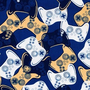 May include: A fabric pattern featuring a repeating design of video game controllers in white, navy blue, and tan against a dark blue background. The controllers have buttons and directional pads.