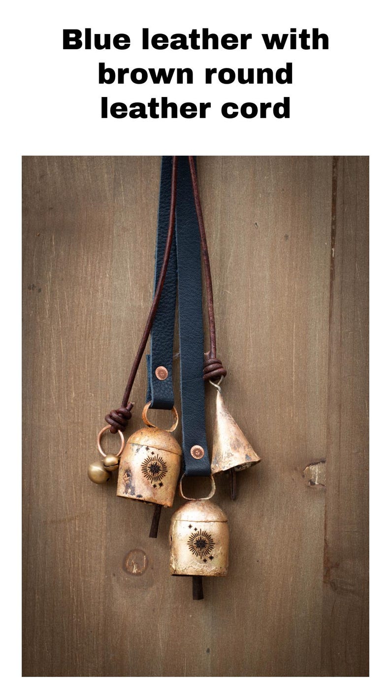 May include: Blue leather straps with brown round leather cords, holding several antique gold bells. The bells have a sunburst design and are hanging against a wooden background.