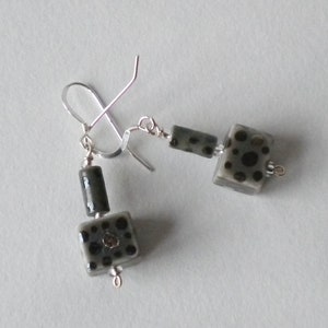 May include: A pair of silver earrings with black and white geometric ceramic beads. The beads have a speckled pattern.