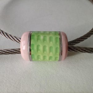 May include: A green and pink cylindrical bead with a patterned design, strung on a silver cable chain.