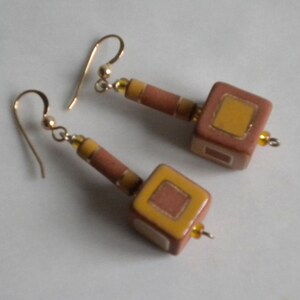 May include: A pair of dangle earrings with brown and yellow geometric ceramic beads. The beads have a square shape with a smaller square inset.