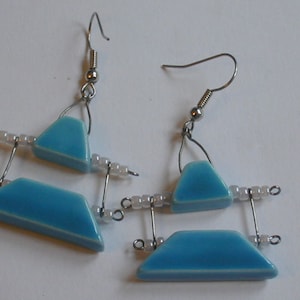 May include: A pair of blue and silver earrings with a geometric design. The earrings are made with small blue ceramic triangles and white beads.