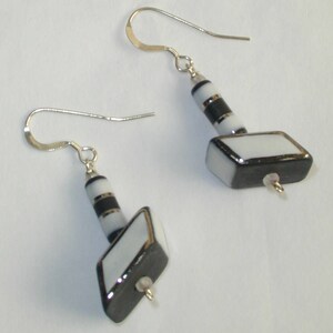 May include: A pair of silver earrings with black and white geometric glass beads. The beads are shaped like a small rectangle with a smaller rectangle attached to the top.