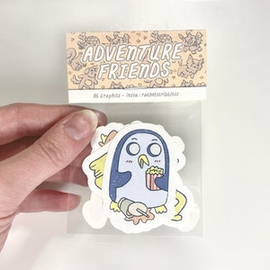 May include: A clear plastic package containing several die-cut stickers. The stickers feature cartoon penguin characters with popcorn and spilled drinks. The package header reads "ADVENTURE FRIENDS" with additional text "RG Graphics - insta: rachelscribbless".