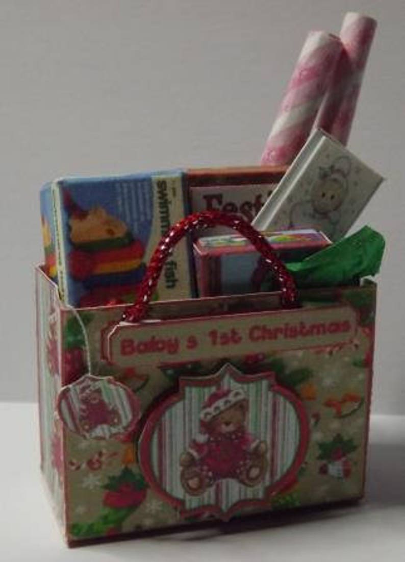 May include: A red and white gift bag with a handle, filled with wrapped gifts and candy canes. The bag has a label that says "Baby's 1st Christmas".