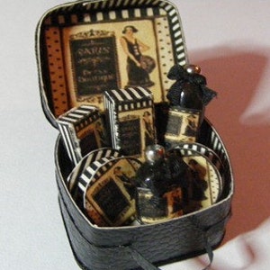 May include: A black faux leather travel case with a black and white striped lining. The case contains a set of miniature perfume bottles, soap bars, and a powder compact. The case has a small handle and a silver clasp.