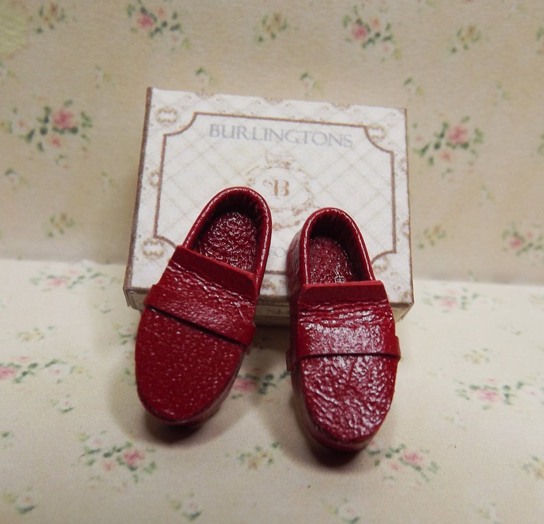 May include: A pair of miniature red leather loafers, resting on a box labelled "Burlingtons".