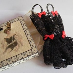May include: A black lace dress with red bows. The dress is in a gift box with a vintage design.