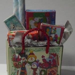 May include: A red and white gift bag filled with wrapped gifts, including a red and white striped gift bag, a blue and white striped gift bag, a red and white gift box, a blue and white gift box, and a red and white gift box. The bag is decorated with a green and white Christmas design featuring snowmen and a Christmas tree.