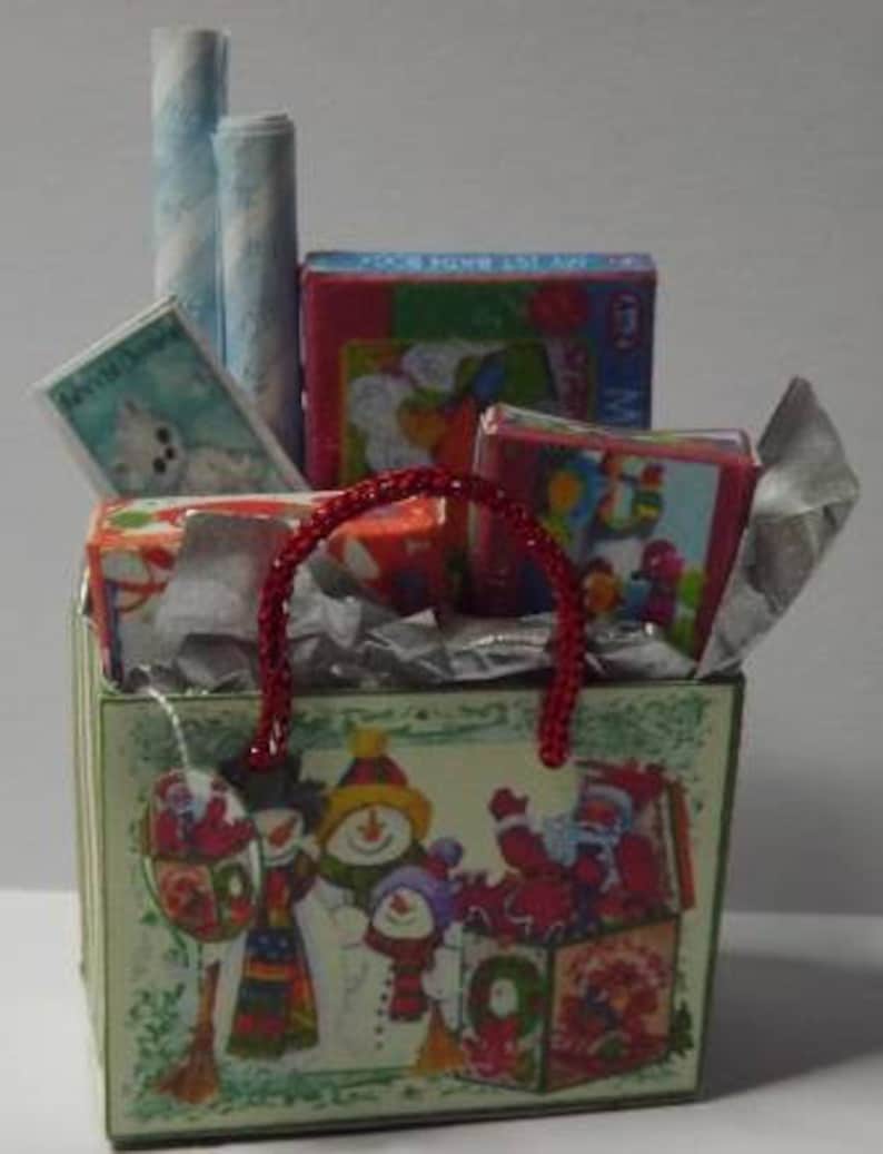 May include: A red and white gift bag filled with wrapped gifts, including a red and white striped gift bag, a blue and white striped gift bag, a red and white gift box, a blue and white gift box, and a red and white gift box. The bag is decorated with a green and white Christmas design featuring snowmen and a Christmas tree.