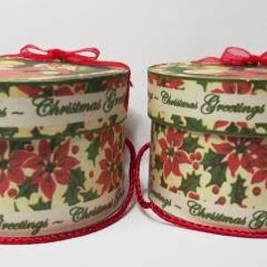 May include: Two round, white gift boxes with red ribbon bows. The boxes are decorated with a green and red floral pattern and the text "Christmas Greetings".